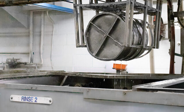 Parts in a metal basket going through a wash surface prep cycle.